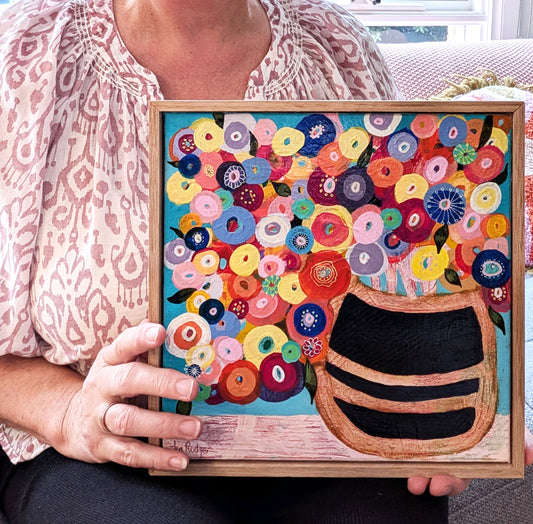 Janet Rodger holding her original acrylic painting of a round vase with colorful circles of flowers