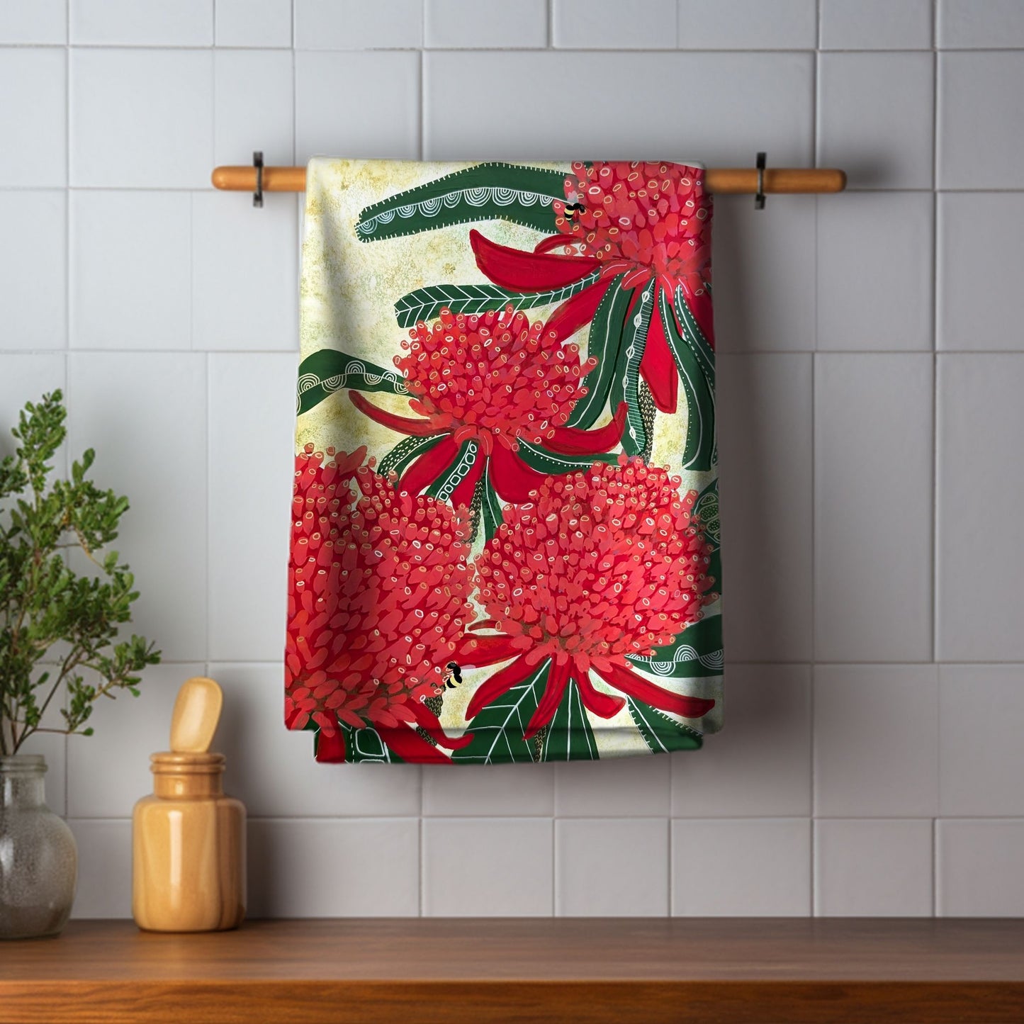 Red Waratah Tea Towel by Jen Rodger Creative hanging on a wooden rack against a tiled wall.