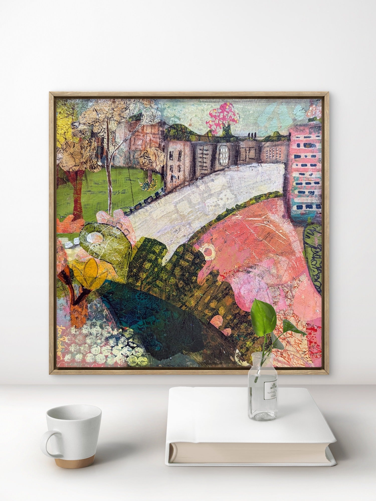 Abstract landscape painting titled The Village on the Hill by Jen Rodger featuring rolling greens and blues with a symbolic village below, representing calm, balance and perspective within the busyness of life. Shown with a desk, book and coffee cup.